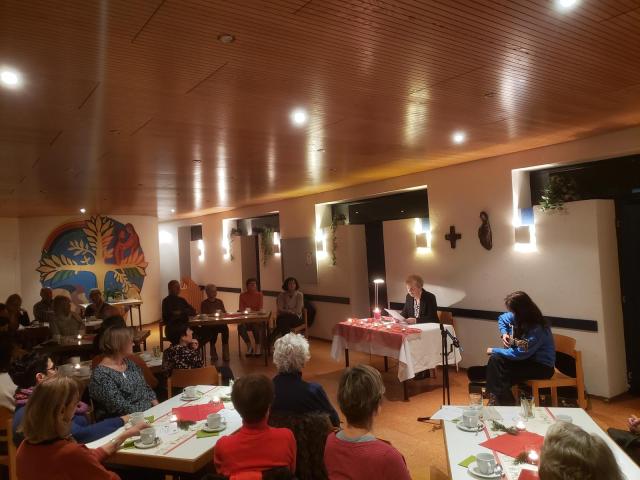 Frau liest Zuhörerinnen Weihnachtstext vor, Raum weihnachtlich geschmückt